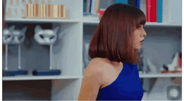 a woman in a blue one shoulder top stands in front of a shelf