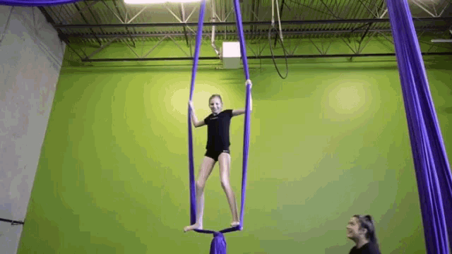 a young girl is hanging from a purple aerial silk