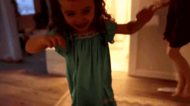 a little girl in a blue dress is dancing in a room while holding a person 's hand .