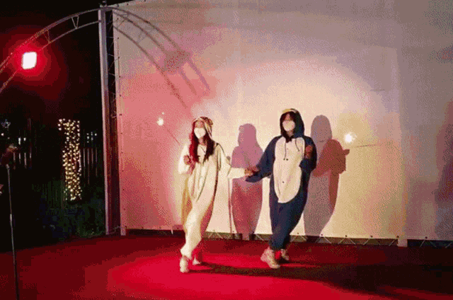 two women in pajamas are dancing on a red carpet while wearing face masks