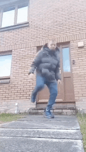 a man in a black jacket is jumping in front of a brick building