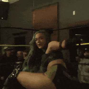 a woman with green hair is in a wrestling ring with a crowd watching