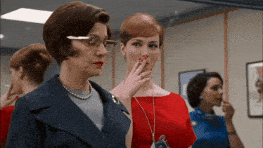 a woman in a red dress is smoking a cigarette next to another woman