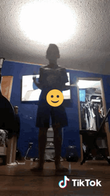 a boy is standing in front of a tv with a smiley face on it and a tiktok logo on the bottom right