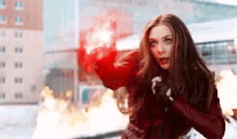 a woman in a red jacket is holding a red object in her hand in front of a fire .