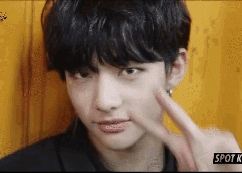 a young man with black hair is making a peace sign with his finger .