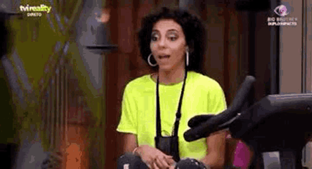 a woman in a neon yellow shirt is sitting on an exercise bike in a gym .