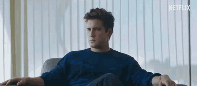 a man in a blue sweater is sitting in a chair in front of a large window .