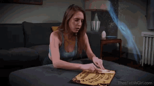 a woman is sitting at a table with a ouija board