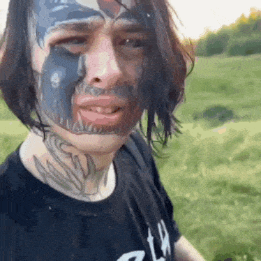 a man with a tattoo on his face is wearing a black shirt with the letter w on it .