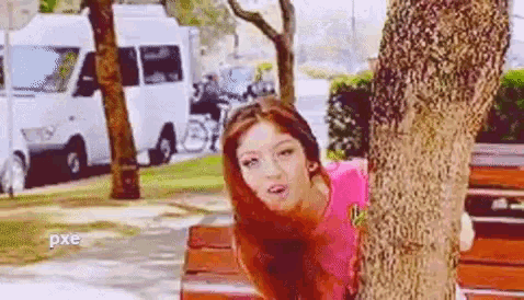 a woman is peeking out from behind a tree in a park