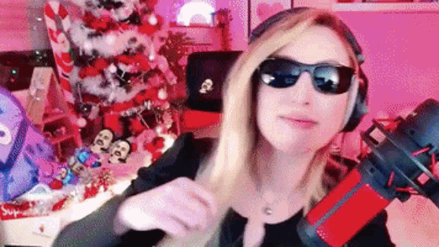 a woman wearing sunglasses and headphones is standing in front of a christmas tree .