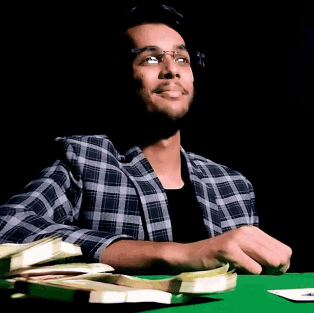 a man in a plaid shirt sits at a table with a stack of money