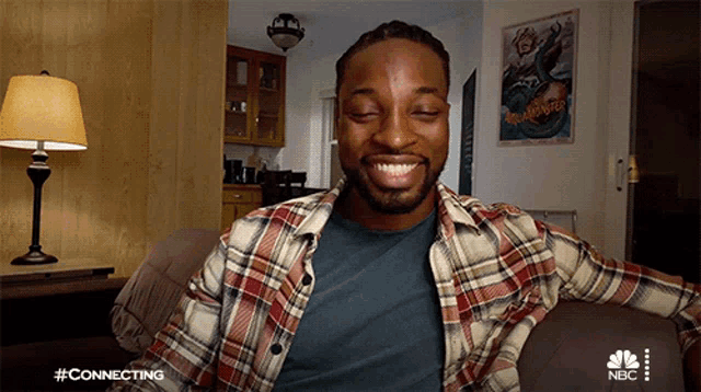 a man in a plaid shirt sits on a couch with a nbc logo on the bottom right