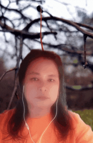 a woman wearing headphones looks at the camera with a tree branch hanging from her head