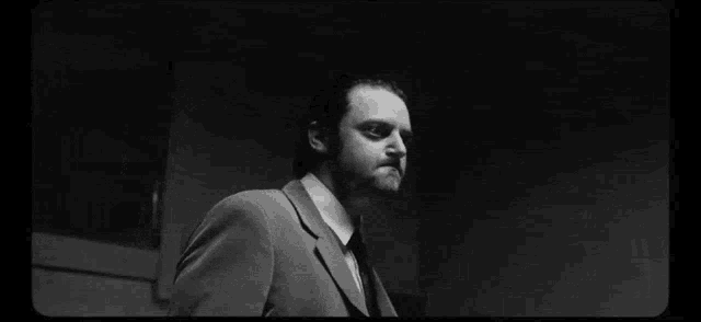 a man in a suit and tie is standing in a dark room giving the middle finger .