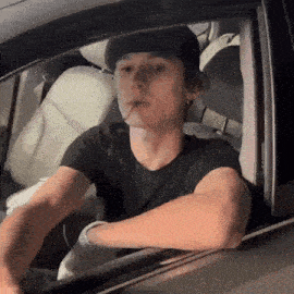 a man in a black hat is smoking a cigarette in a car .