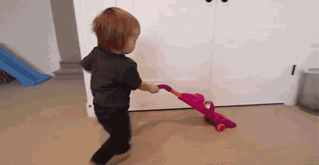 a young boy is playing with a toy vacuum cleaner on the floor .