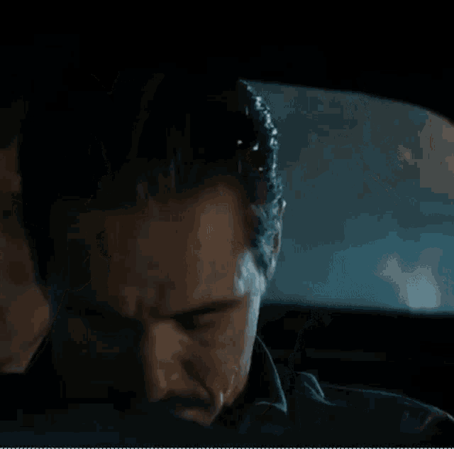 a man is covering his mouth with his hands while sitting in a car at night .