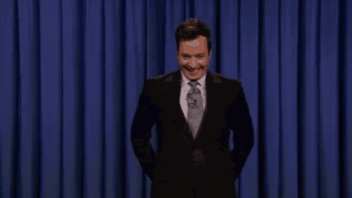 a man in a suit and tie is standing on a stage with his hands in his pockets and smiling .