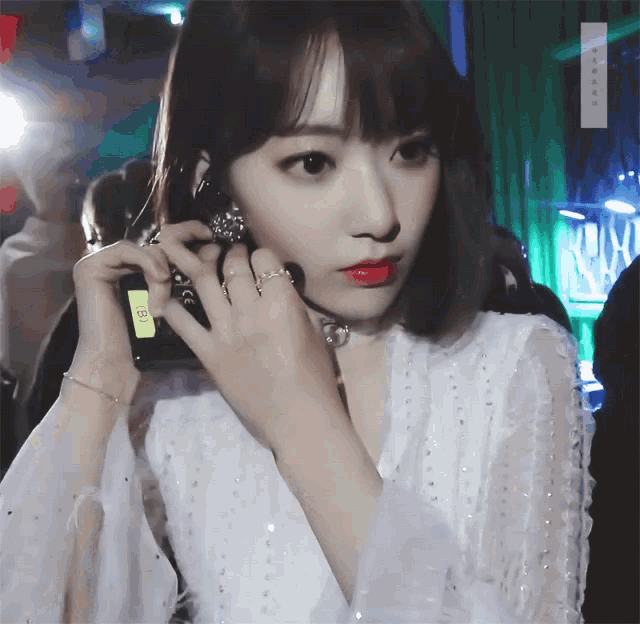 a woman in a white dress is holding a cell phone with a yellow tag that says ' cc ' on it