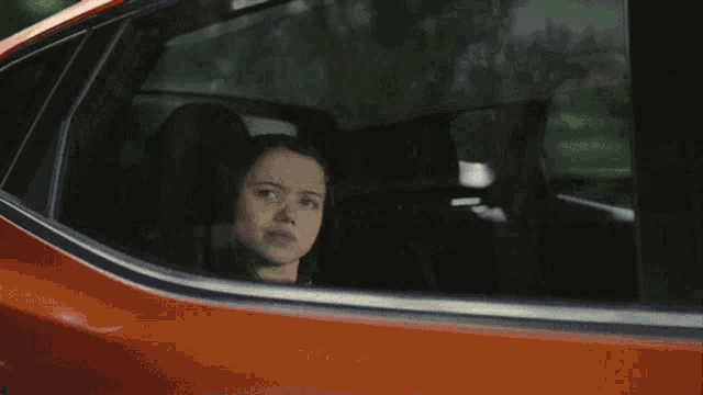 a young girl is looking out of the window of an orange car