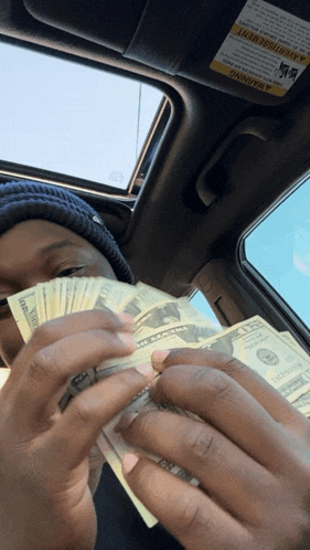 a person in a car holding a bunch of money with a warning sticker on the visor