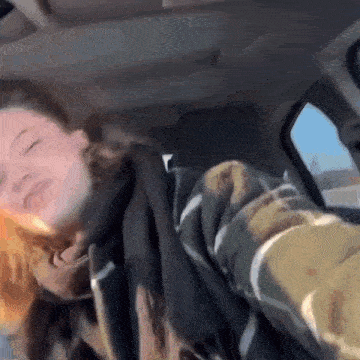 a woman is sitting in the back seat of a car holding a slice of pizza .