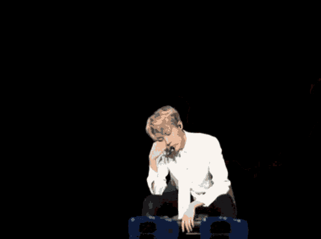 a man in a white shirt and bow tie is sitting on a chair with his legs crossed