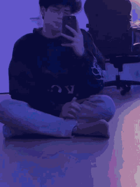 a young man is sitting on the floor taking a picture of himself with his phone .