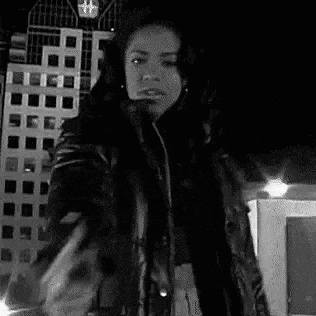 a black and white photo of a woman in a leather jacket pointing a gun at the camera .