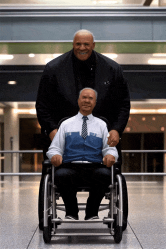 a man in a suit is standing next to another man in a wheelchair