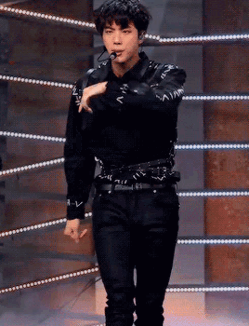 a young man wearing a black shirt and black pants is standing in front of a microphone