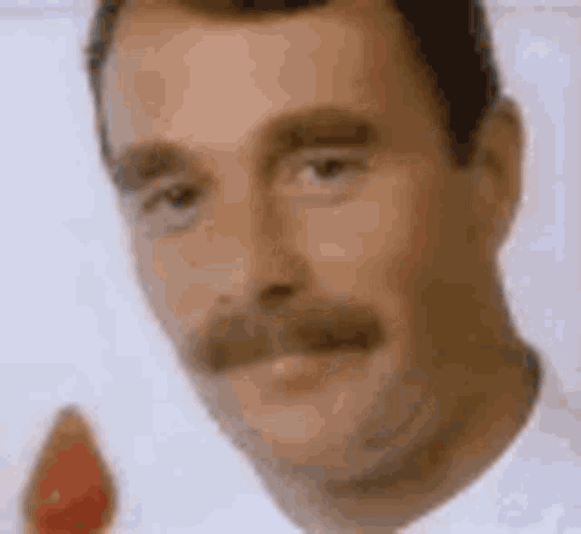 a close up of a man 's face with a mustache holding a strawberry .