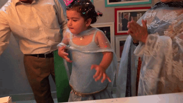 a little girl in a blue dress stands in front of a man and woman