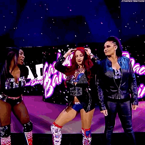 three women are standing next to each other on a stage in a purple room .