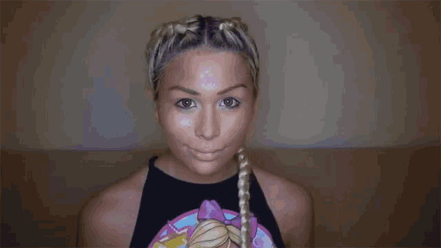 a woman with blonde hair and braids is wearing a black tank top with a picture of a barbie on it .