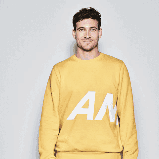 a man wearing a yellow sweatshirt with the letter an on it gives a thumbs up