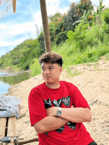 a man wearing a red t-shirt with a black cat on it stands with his arms crossed