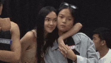 a girl is hugging another girl in a crowd while a man looks on .