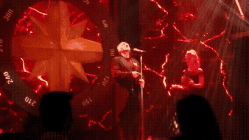 a man singing into a microphone on a stage with a red background