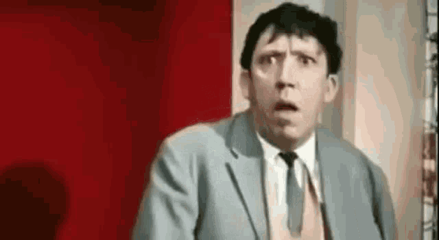 the man is wearing a suit and tie and making a surprised face .