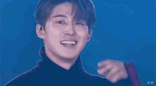 a young man is smiling and pointing at the camera while wearing a black turtleneck .