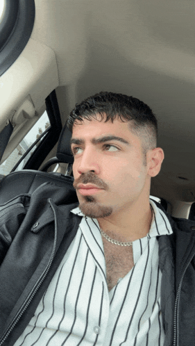 a man in a striped shirt and a black jacket is sitting in the back seat of a car