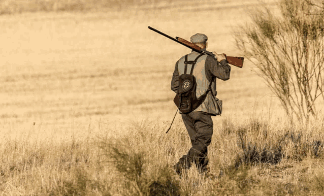 a man is carrying a rifle in a field and has a bag on his back that says ' a. '