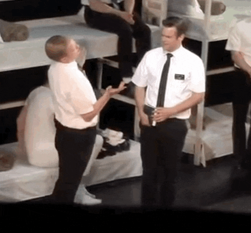 a man with a name tag on his shirt talks to another man in a white shirt and tie