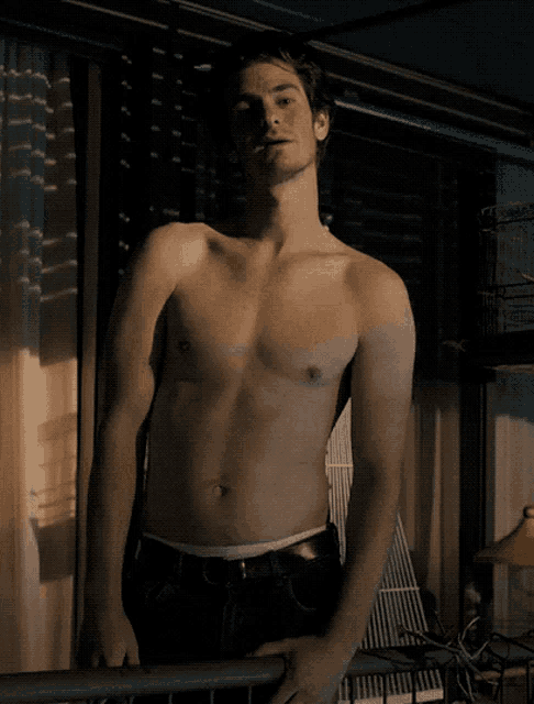 a shirtless man stands on a balcony with his hand on the railing