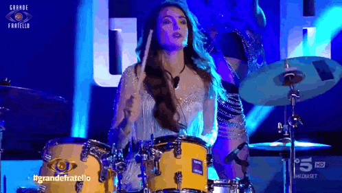 a woman is playing drums on a stage in front of a sign that says grande fratello on it