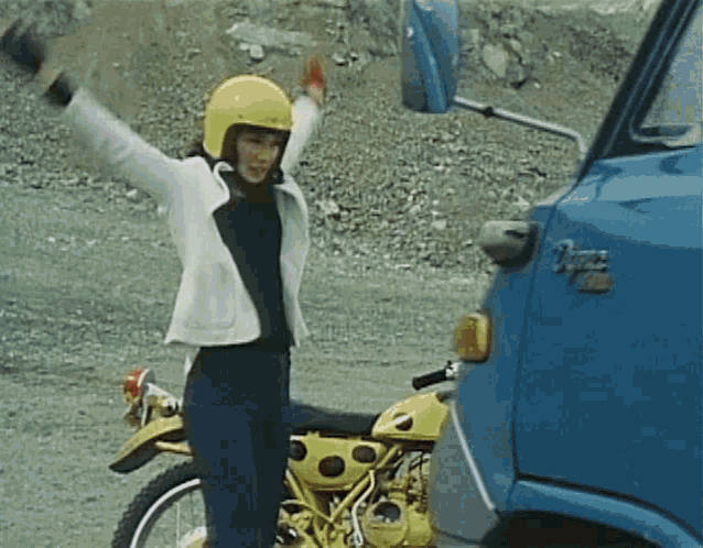 a woman in a yellow helmet is standing next to a motorcycle and a blue truck .