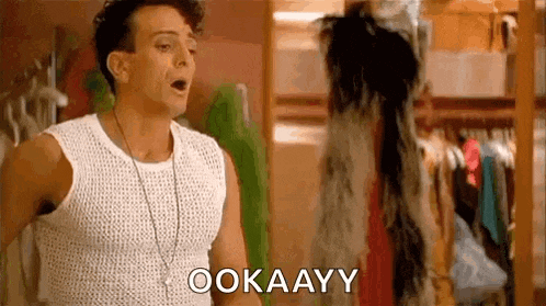 a man in a white tank top is standing in front of a closet and saying okay .